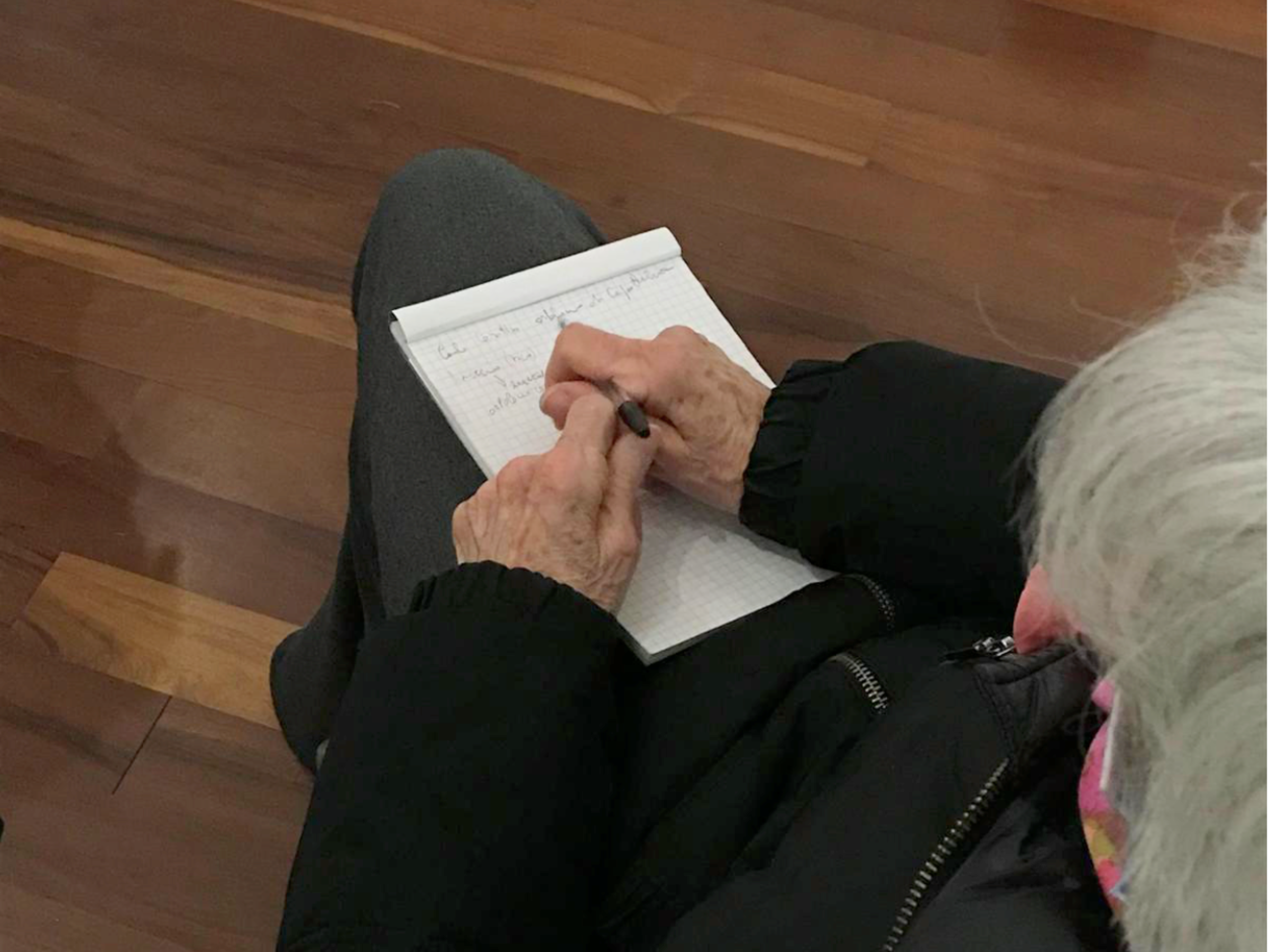 Una donna anziana seduta scrive a penna sul suo taccuino
